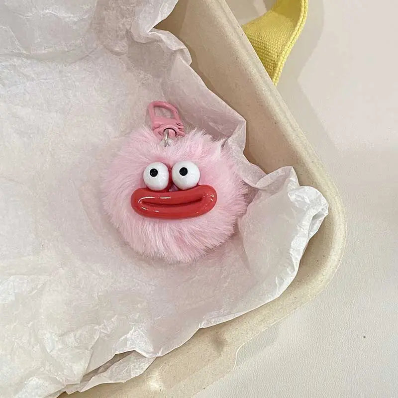 A pink fluffy sausage mouth plush keychain charm is shown resting in white tissue paper inside a light-colored container.