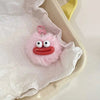 A pink fluffy plush sausage with a red mouth and a pink keychain hanging in white tissue paper.