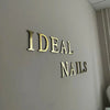 Gold acrylic mirror letter wall stickers spelling IDEAL NAILS mounted on a light gray wall