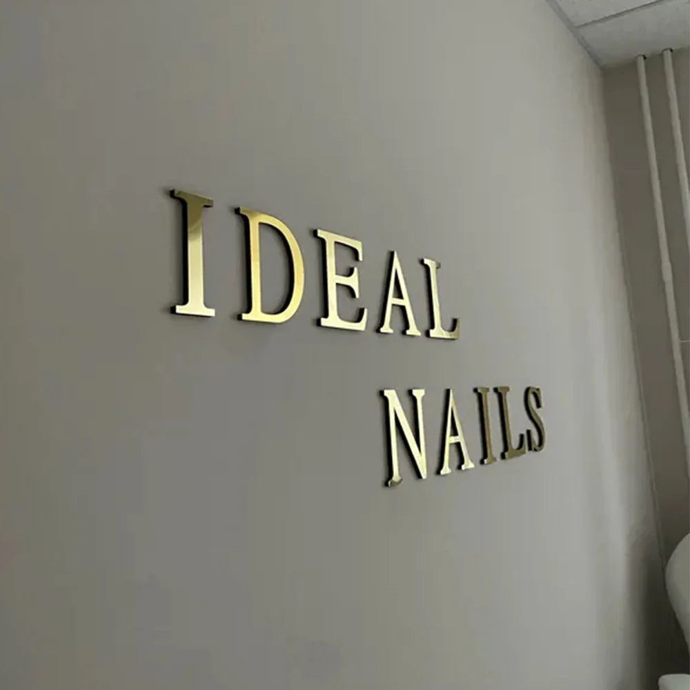 Gold acrylic mirror letter wall stickers spelling IDEAL NAILS mounted on a light gray wall