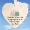 A heart-shaped sea glass ornament featuring a white tree silhouette and two small, translucent figures.
