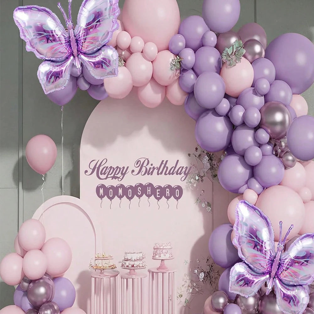 A pink and purple balloon garland arch featuring balloons and a purple butterfly decoration for a birthday celebration.