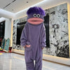 A purple monster onesie pajama set with large pink eyes and a stitched mouth stands in a modern room.