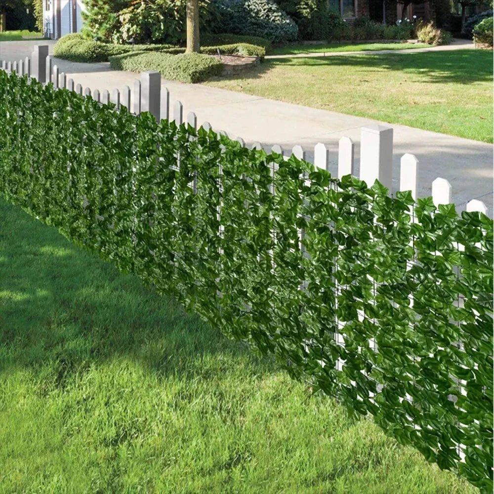 A long row of artificial ivy hedge fence panels lining a walkway and lawn.