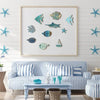 A set of ten wooden hanging fish decorations in various shades of blue and teal displayed on a white wall above a striped sof