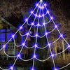 A glowing purple spider web light installation illuminates a tree in a dark outdoor setting.