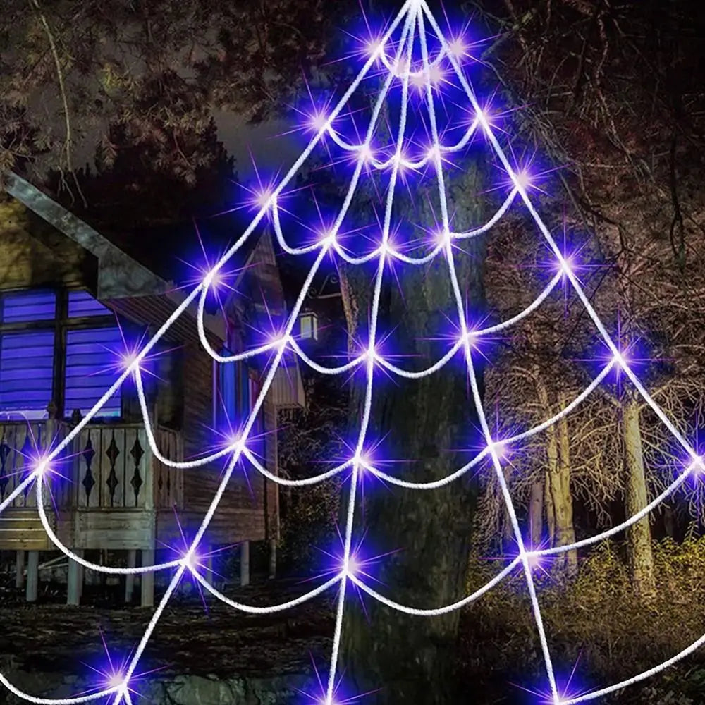 A glowing purple spider web light installation illuminates a tree in a dark outdoor setting.