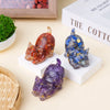 Three natural crystal cat statues in shades of amber, blue, and purple displayed on white blocks.