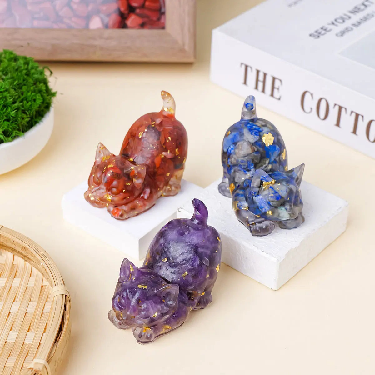 Three natural crystal cat statues in shades of amber, blue, and purple displayed on white blocks.