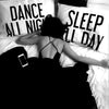 A person lying in bed with black and white text pillows reading Dance All Night and Sleep All Day.