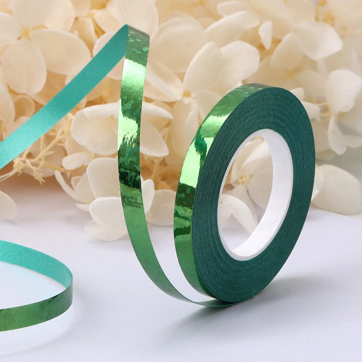 Roll of green satin balloon ribbon spiraling against a background of white flowers.