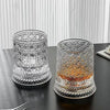 A clear crystal whiskey glass with a relief design sits on a dark surface.