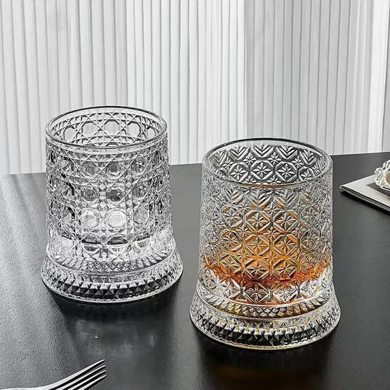 A clear crystal whiskey glass with a relief design sits on a dark surface.