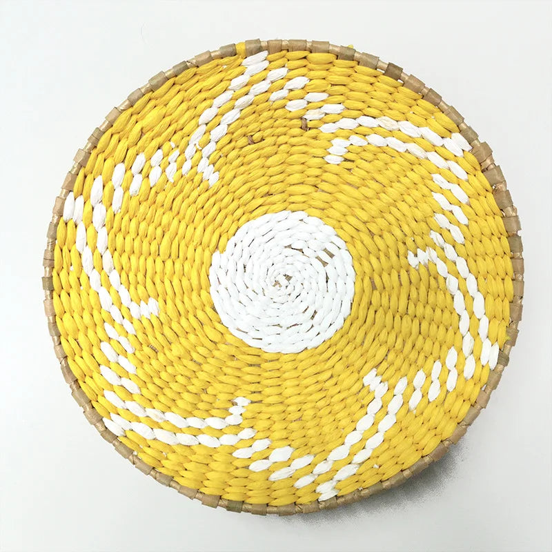 Round woven straw wall decor hanging in yellow and white with a central circular pattern