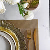 Elegant gold charger plates with textured rims and gold cutlery set on a neutral linen napkin.