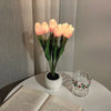 A bouquet of glowing peach-colored tulips in a white ceramic pot used as a night light.