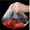 A hand is holding a clear plastic elastic food cover filled with fresh red tomatoes.