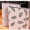 A close-up of a beige linen photo album with green botanical illustrations, resting on a wooden surface.
