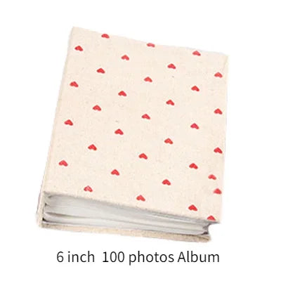 A beige photo album with a light pattern of red hearts, measuring 6 inches and holding 100 photos.