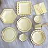 A collection of gold disposable party tableware including plates, napkins, cups, and straws arranged on a light surface.