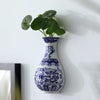 Antique blue and white ceramic wall vase holding green foliage against a white background.