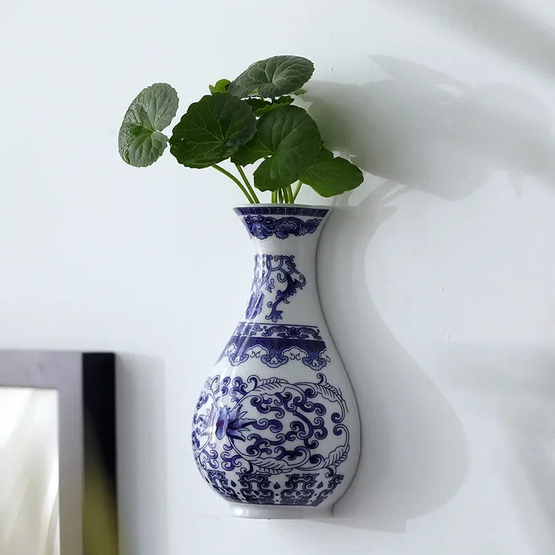 Antique blue and white ceramic wall vase holding green foliage against a white background.