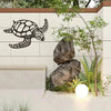 Black metal sea turtle wall art mounted on a light-colored wall with natural greenery and rocks.
