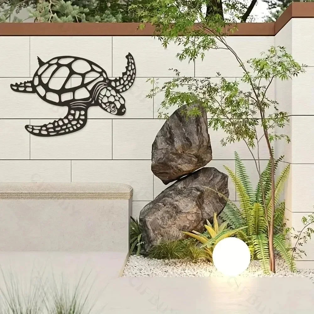 Black metal sea turtle wall art mounted on a light-colored wall with natural greenery and rocks.