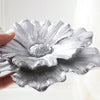 A hand holds a silver gray flower-shaped resin wall art piece against a bright background.