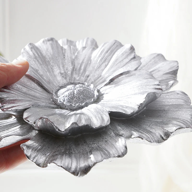 A hand holds a silver gray flower-shaped resin wall art piece against a bright background.