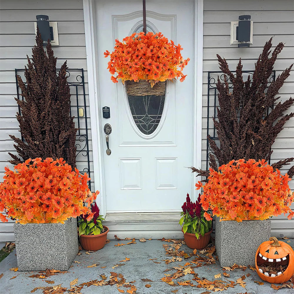 Two potted artificial orange and red flowers flank a white door decorated with dark foliage.