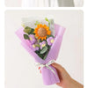 A purple bouquet of handcrafted crochet sunflowers and daisies tied with a white ribbon.