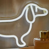 A white neon sign shaped like a dog is displayed on a surface next to a glass bottle.