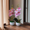 A pair of realistic artificial orchid potted plants with pink and purple flowers displayed on a wooden surface.