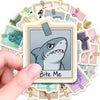 A hand holds a white vinyl sticker featuring a gray shark face with a menacing expression.