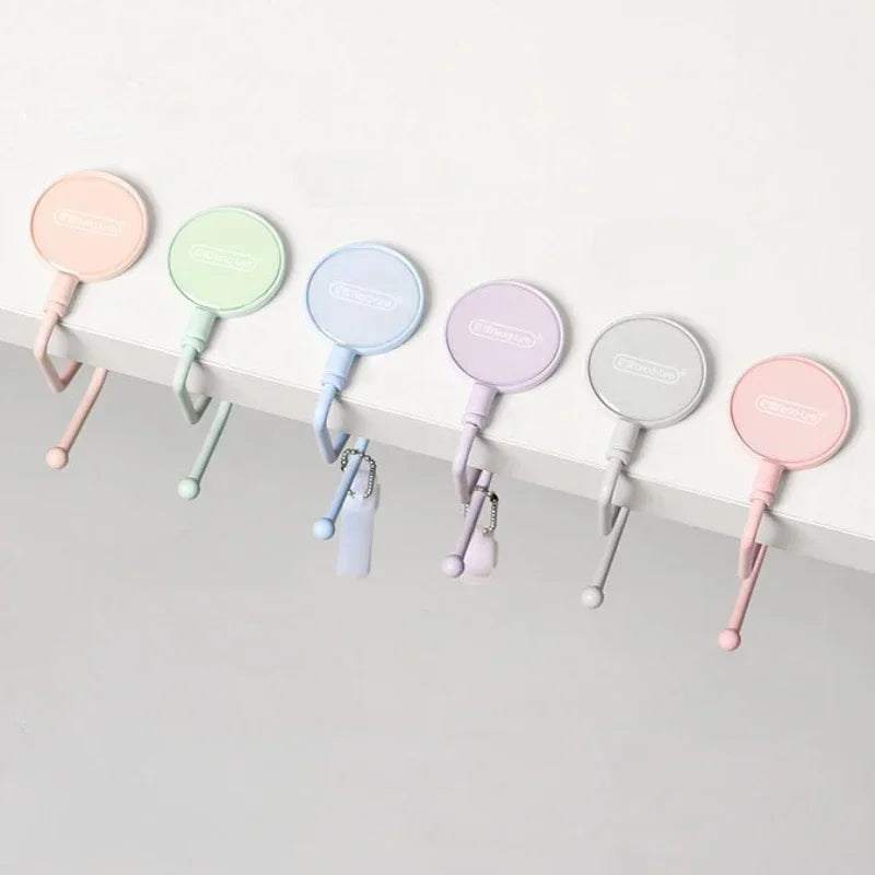 A row of colorful heavy duty purse and bag hooks in pink, mint green, and light blue hanging against a white surface.