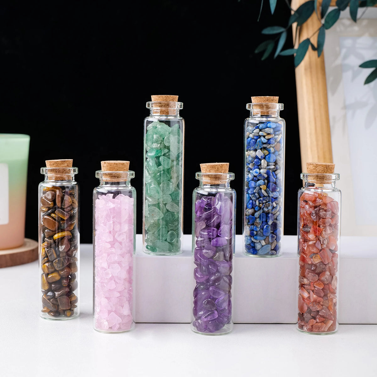 A collection of natural crystal healing stones in glass bottles featuring various colors like green, pink, purple, and blue.