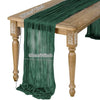 A sage green semi-sheer gauze table runner draped over a wooden table.