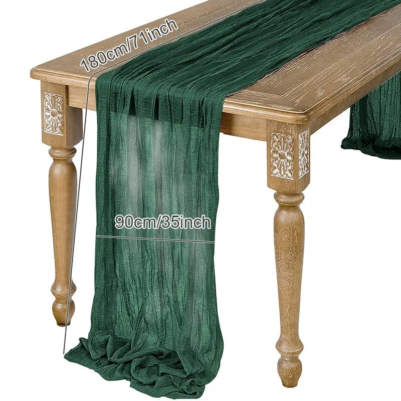 A sage green semi-sheer gauze table runner draped over a wooden table.