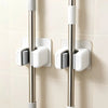 Three silver wall holders with white grips for storing mops, brooms, and long-handled tools.