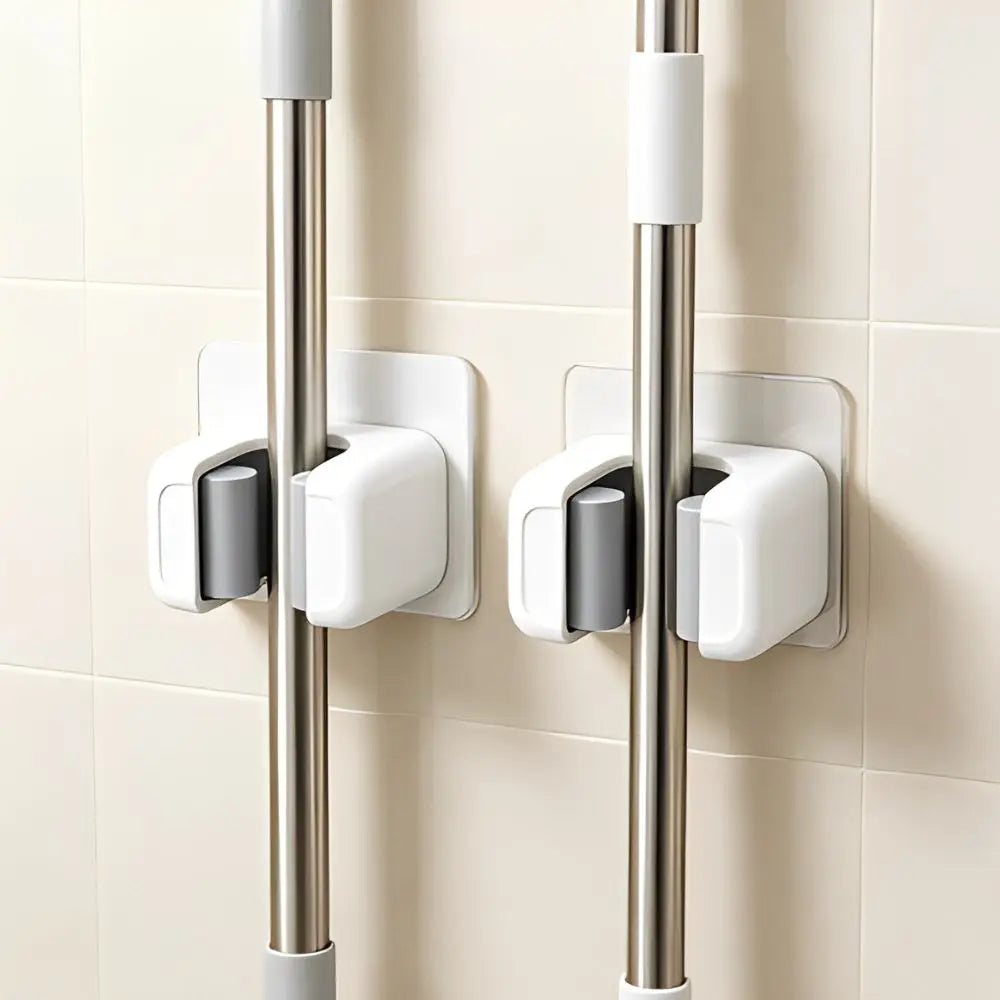 Three silver wall holders with white grips for storing mops, brooms, and long-handled tools.