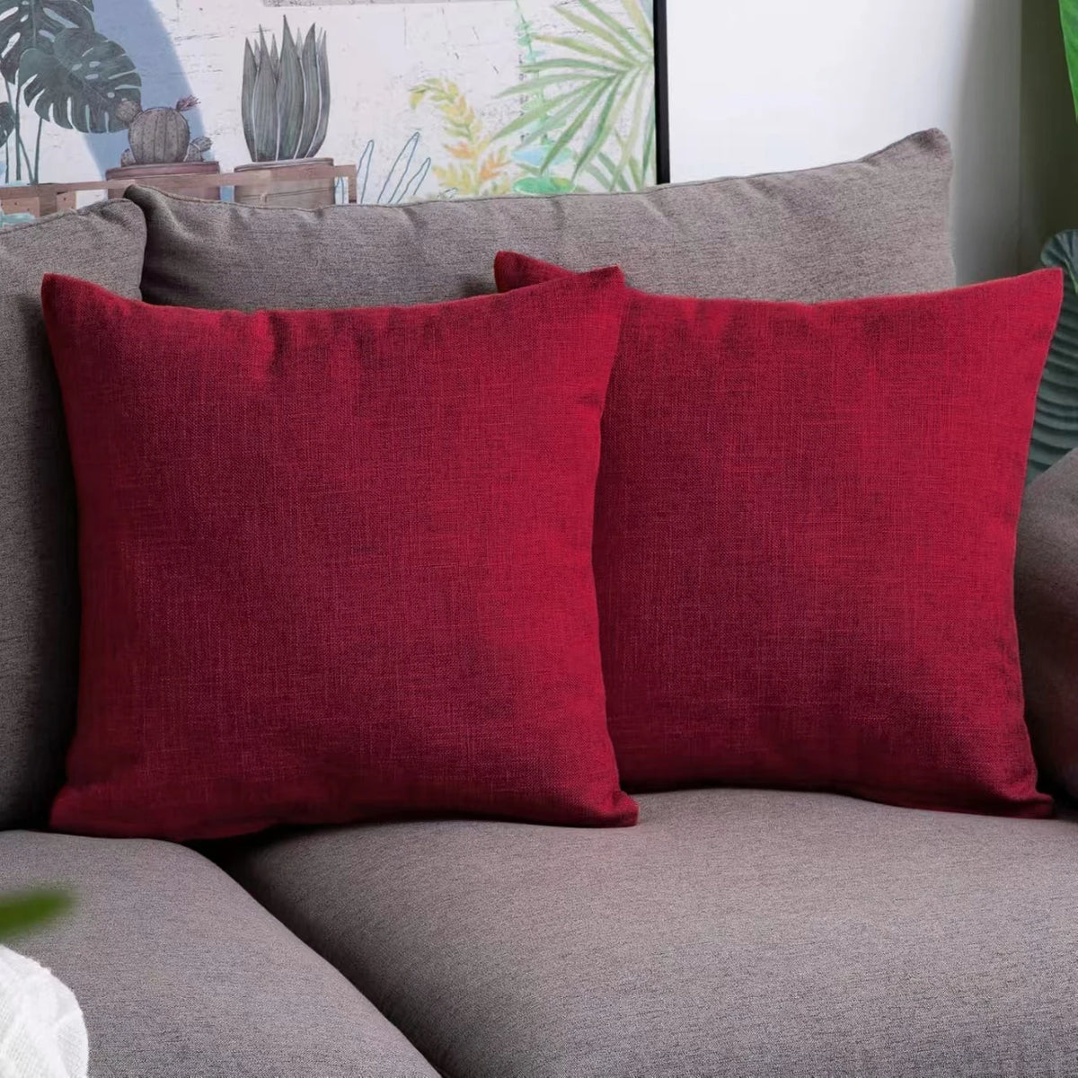 A set of two solid red linen pillows resting on a gray sofa.