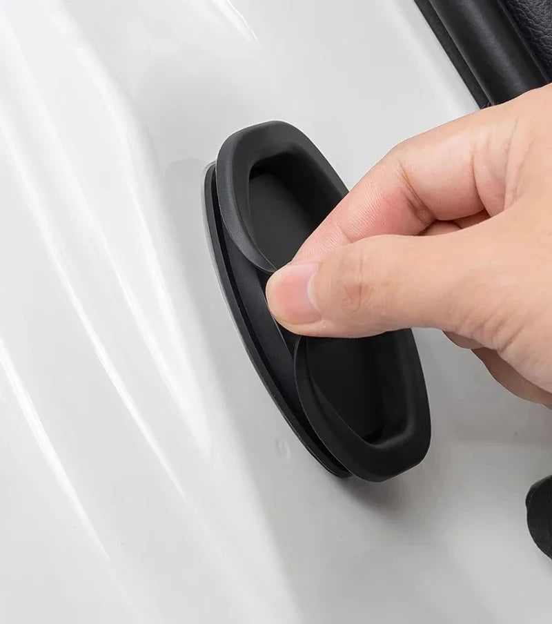 A hand is pressing a black silicone door lock protector onto a white car door surface.