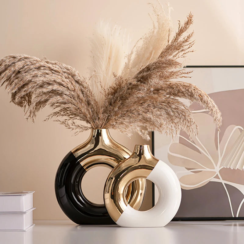 Two gold and black ceramic rings holding dried beige pampas grass flowers on a white surface.