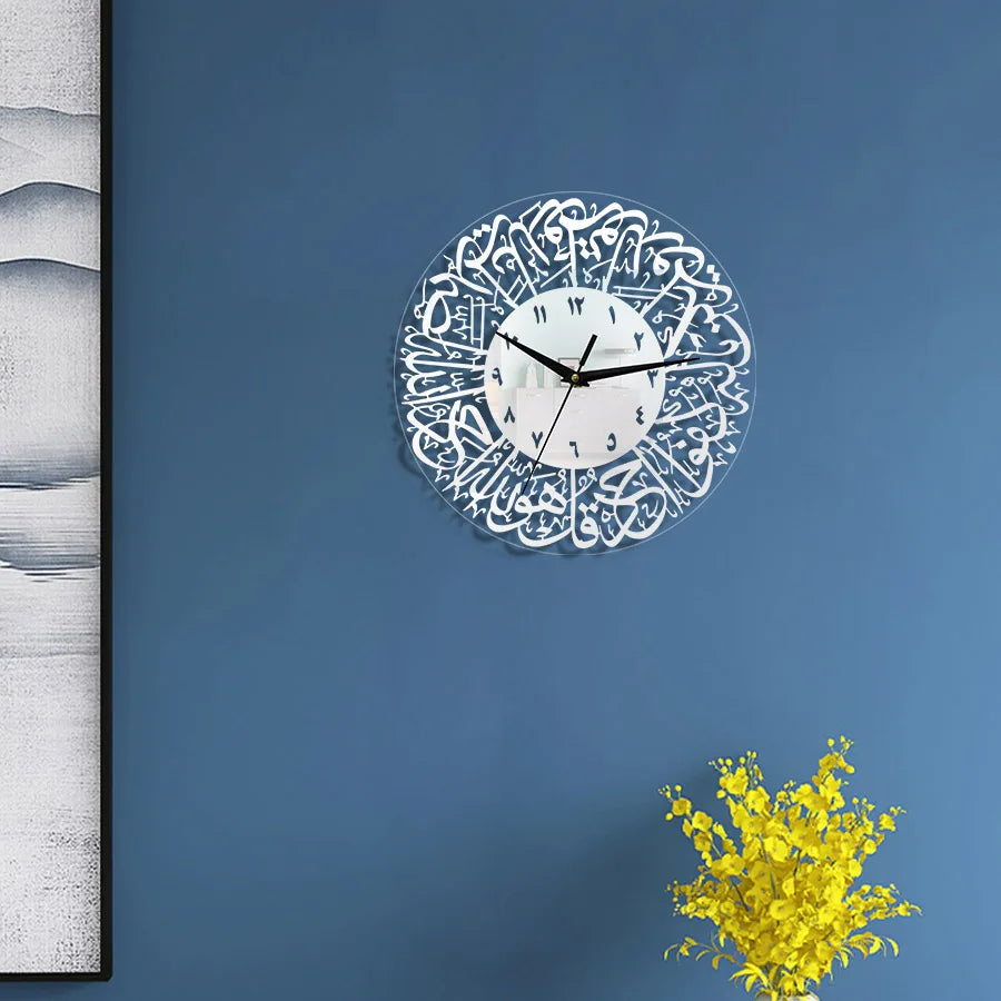 A round acrylic wall clock with Arabic calligraphy and a white face is mounted on a blue wall next to a vertical piece of art