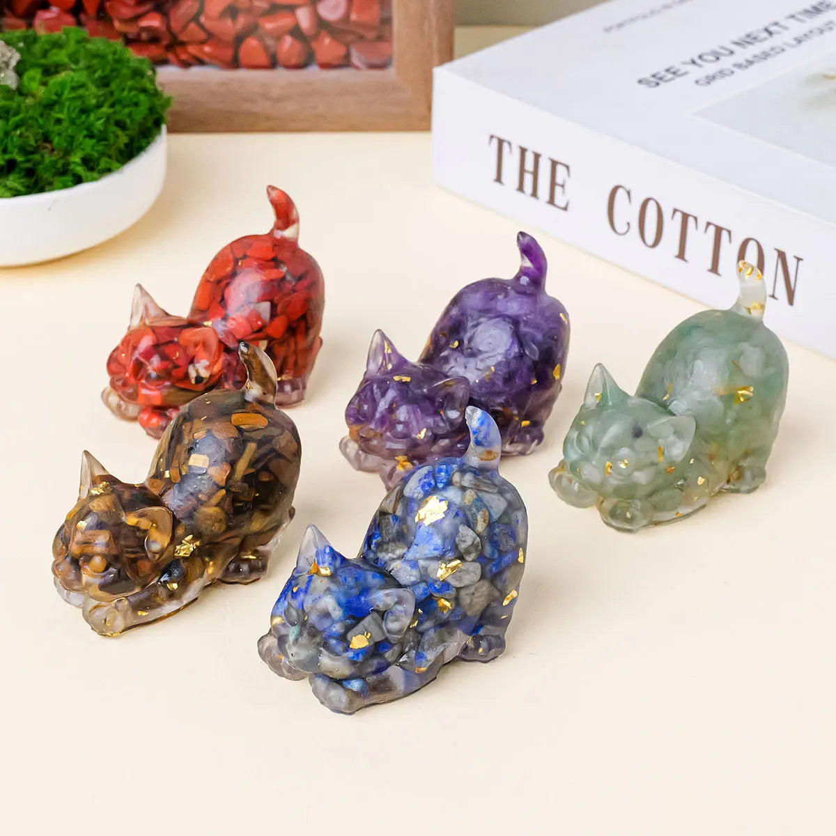 A collection of natural crystal cat statues in various colors including red purple green and blue displayed on a light backgr