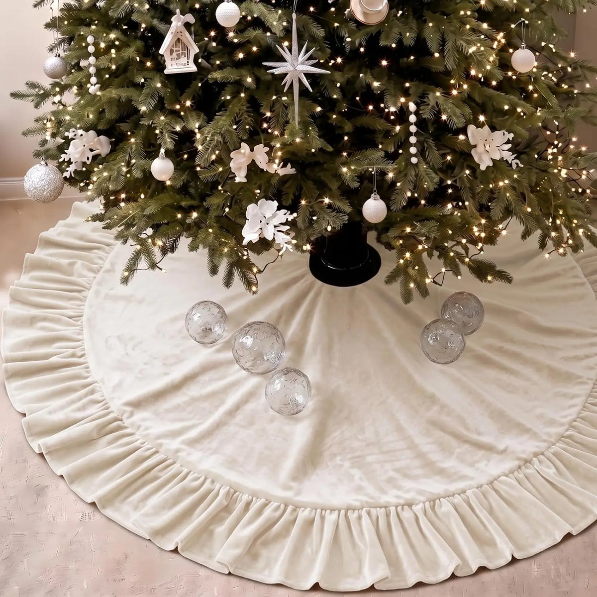 A green Christmas tree decorated with lights and ornaments sits on a white velvet skirt with a ruffled edge.