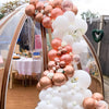 A large balloon garland featuring rose gold and white balloons is displayed outdoors.