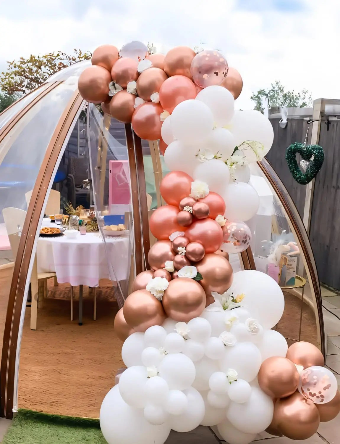 A large balloon garland featuring rose gold and white balloons is displayed outdoors.
