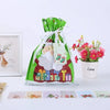 A green drawstring gift bag featuring Santa and snowman designs, next to a potted pink flower plant.